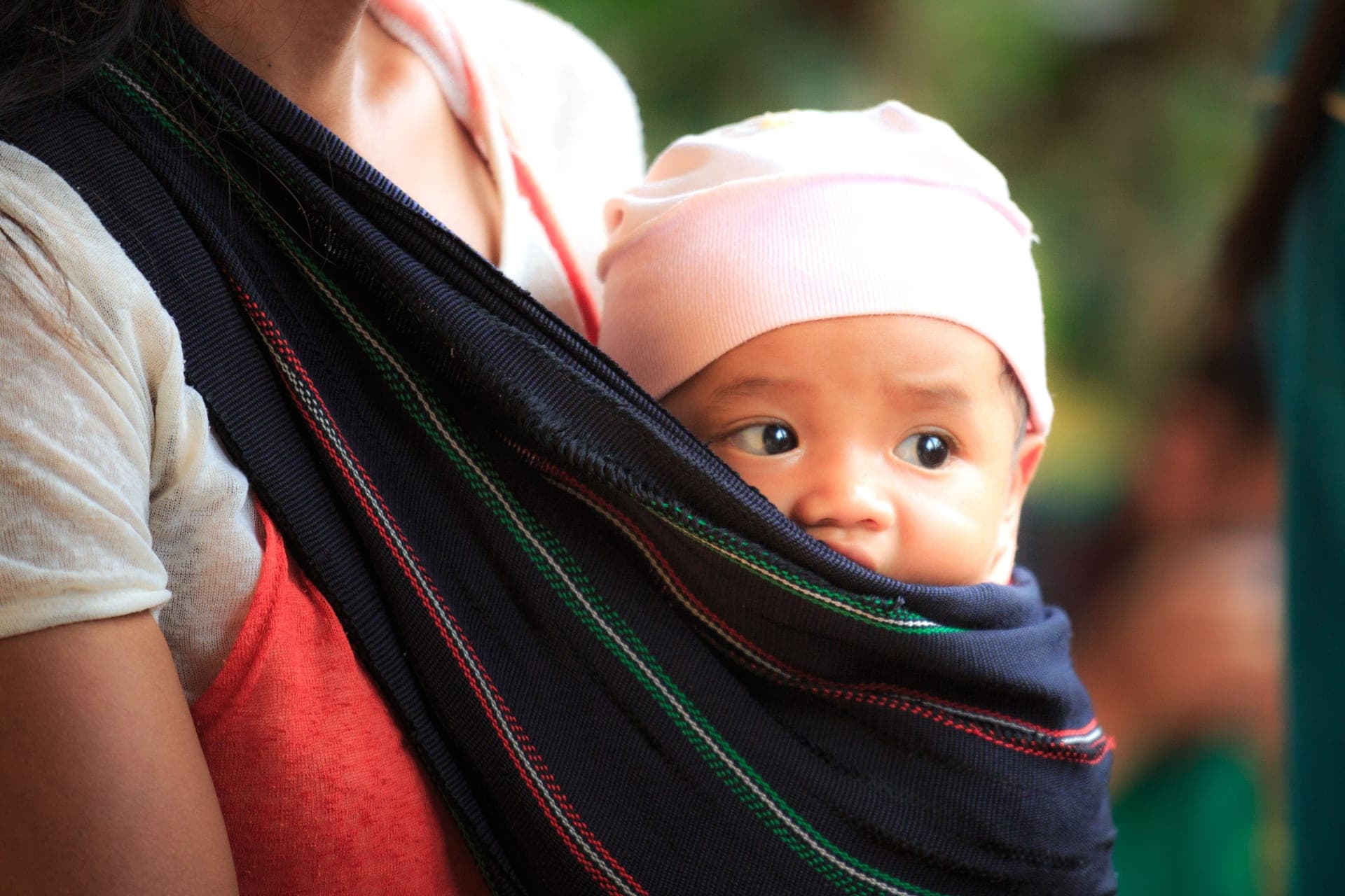 A parent walking outdoors with a baby held against their chest in a fabric carrier