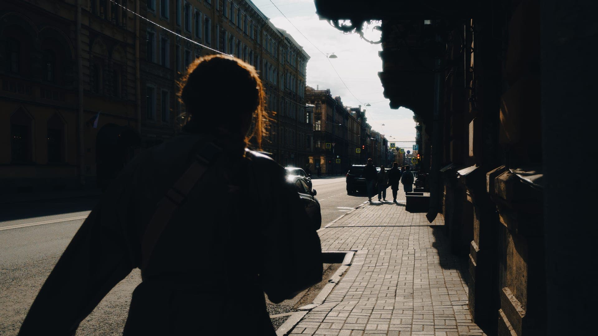 A traveler carrying a backpack on one shoulder while walking down a city street